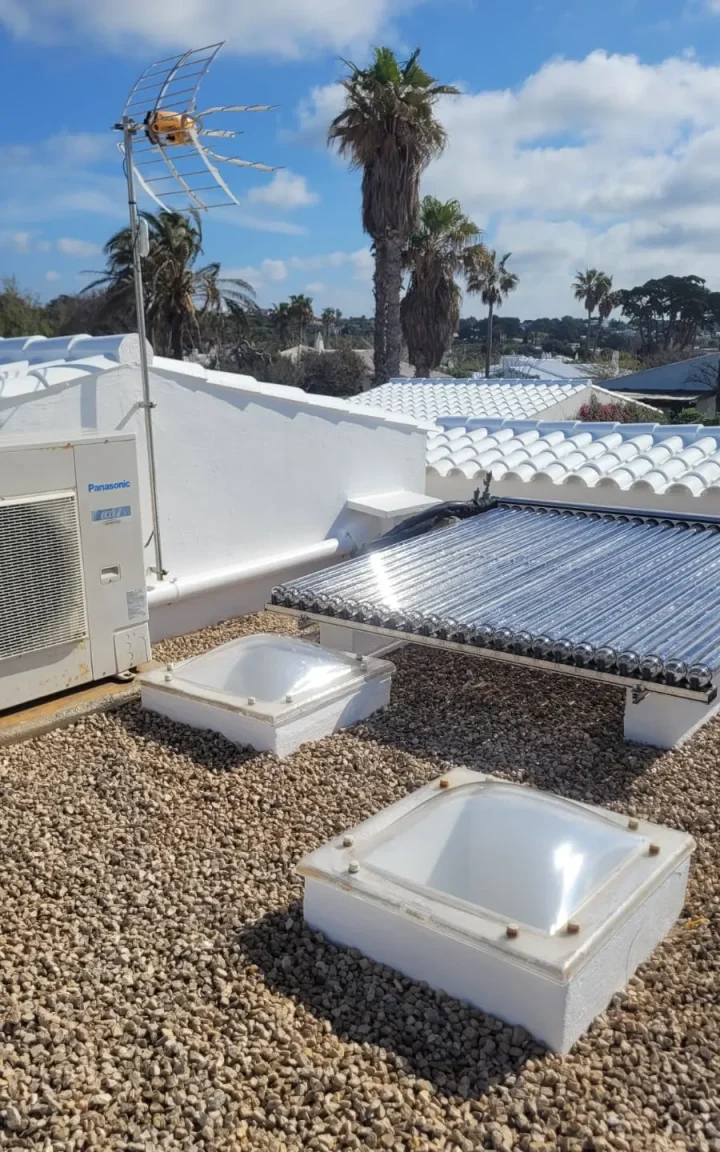 Azotea con claraboyas y pretiles repintados en blanco junto a placas solares