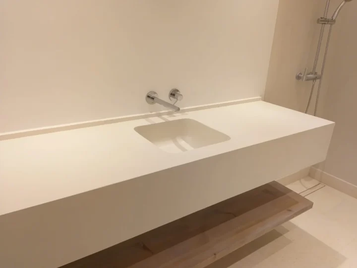 Encimera blanca suspendida con lavabo integrado y grifo empotrado en la pared, sobre balda de madera