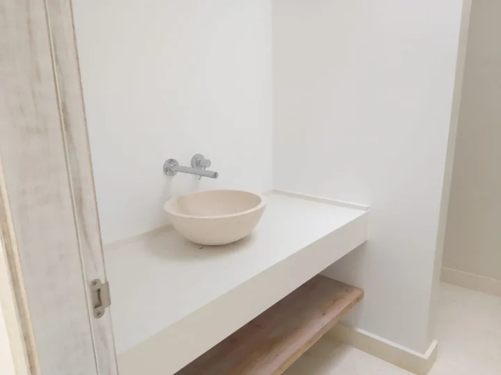 Lavabo de piedra sobre encimera blanca con grifo de pared y paredes lisas blancas