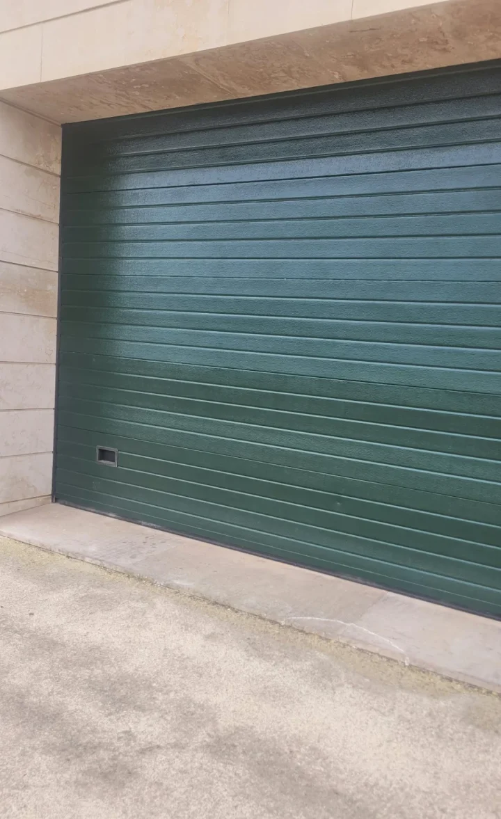 Puerta de garaje seccional repintada en verde oscuro, con acabado uniforme