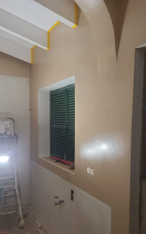 Pared de microcemento en color arena junto a ventana con persiana verde menorquina