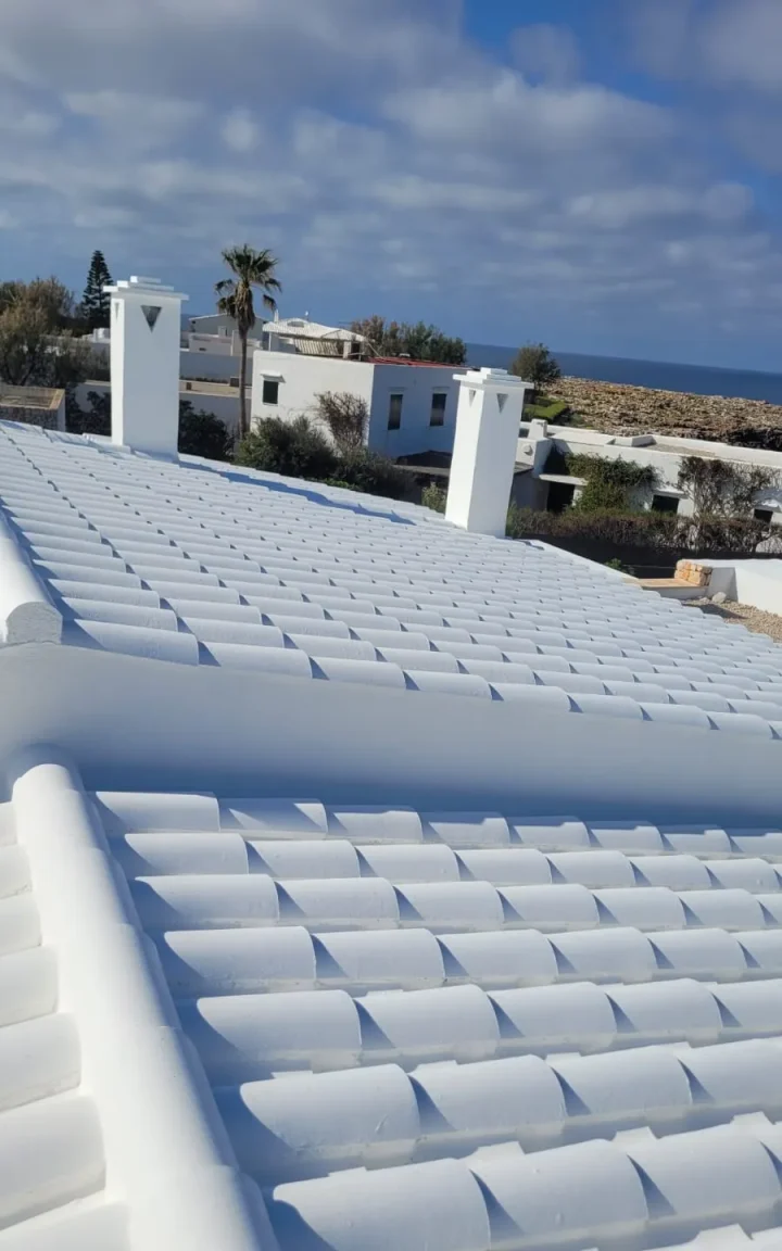 Tejado de teja árabe pintado en blanco menorquín con chimeneas y vistas al mar